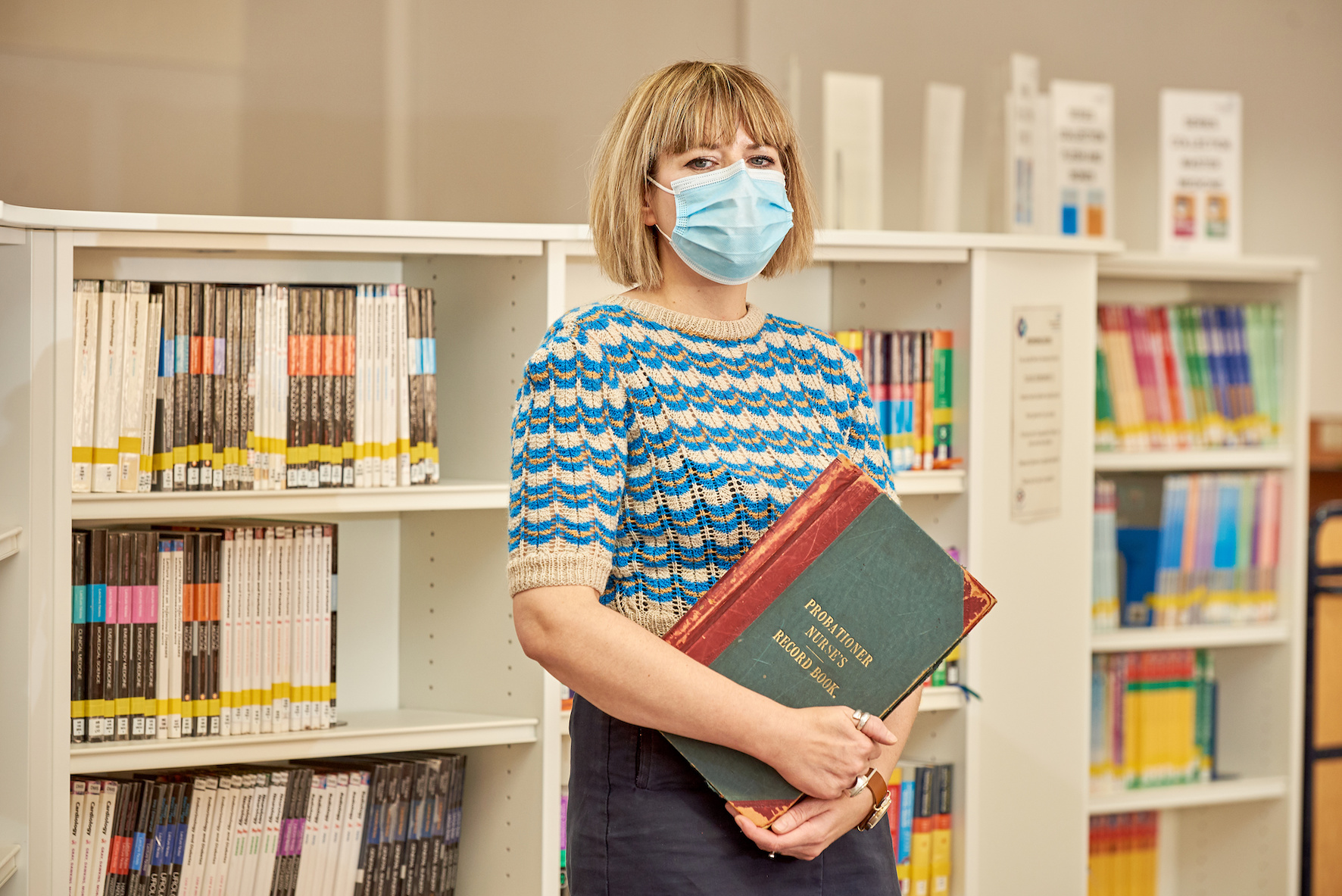 A member of the library team standing in front of bookshelves holding a book.