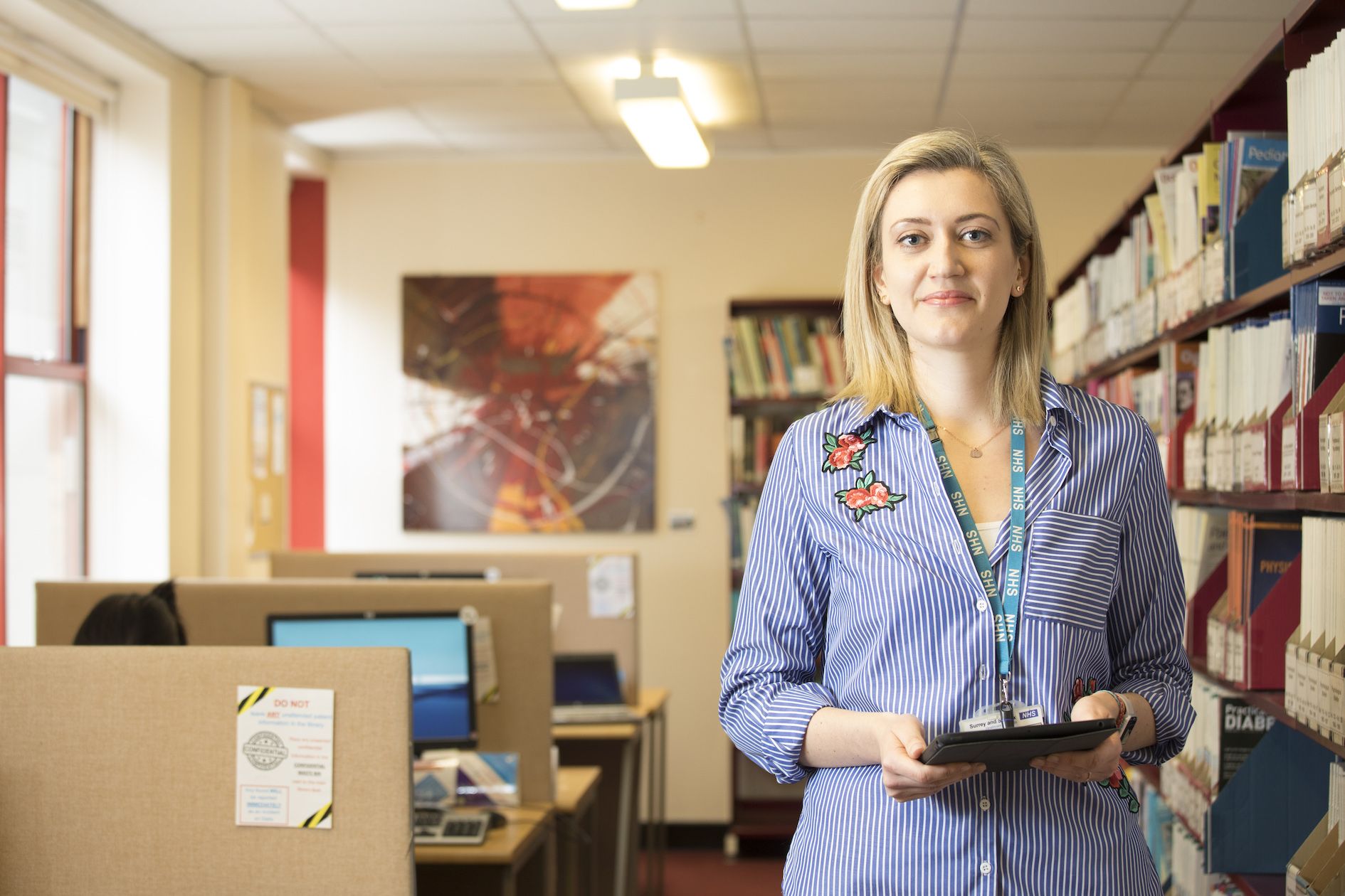 A female library professional with blonde hair holding a book in a library.