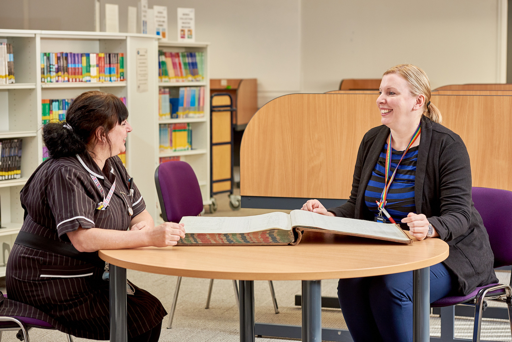 An image of 2 females sitting at a table in a library having a discussion.
