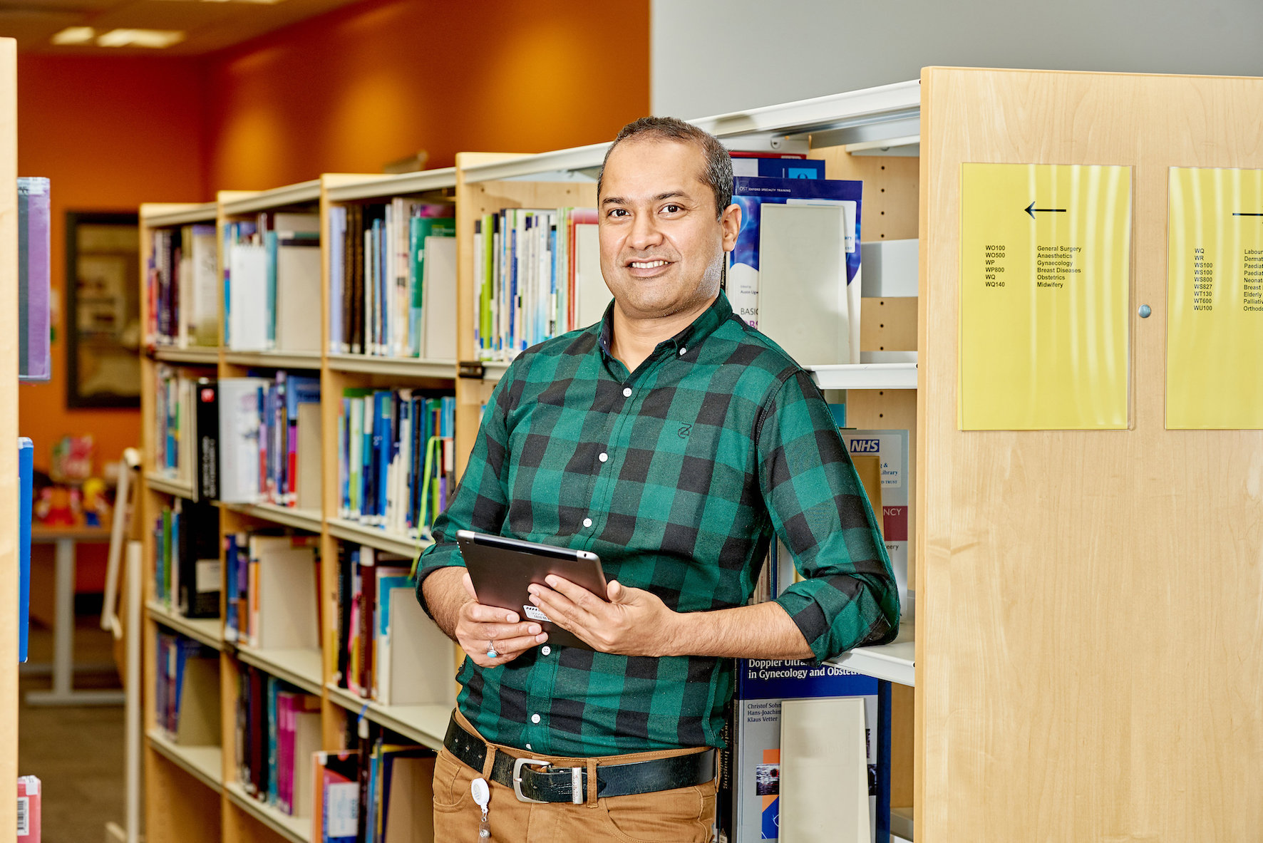 A male library professional holding a book standing in front of a bookshelf.